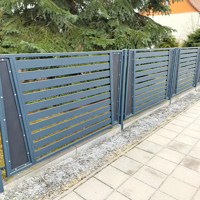 Stahlzaun mit geometrischen Holzelementen und stabiler Betonverankerung auf einem großen Grundstück